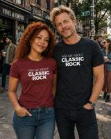 A man and a woman standing on a city street wearing matching graphic t-shirts with the text 'ASK ME ABOUT CLASSIC ROCK'. The woman's shirt is maroon, and the man's shirt is black.