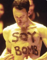 Man with 'SOY BOMB' written on his chest against a dark background