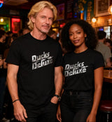 Two people wearing 'Ducks Deluxe' shirts in a bar setting